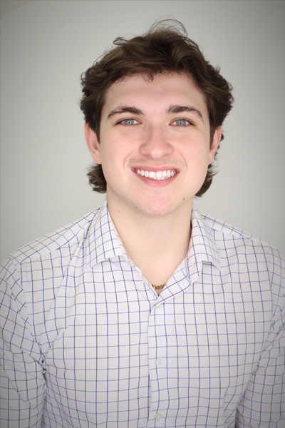 Studio portrait of a person wearing a light-colored checkered button-down shirt against a neutral background
