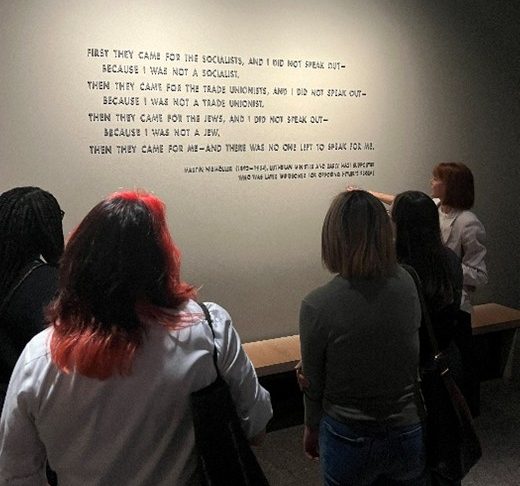 Students gather at the United States Holocaust Memorial Museum in Washington, D.C., reading the iconic Martin Niemöller quote displayed on a gallery wall, which begins: "First they came for the socialists, and I did not speak out — because I was not a socialist."