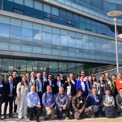 Participants in the Industry Summit on Artificial Intelligence for the Built Environment pose for a group photo outside the Syracuse Center of Excellence building on a sunny day.