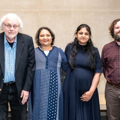 Four people pose together for a photo at an indoor academic event.