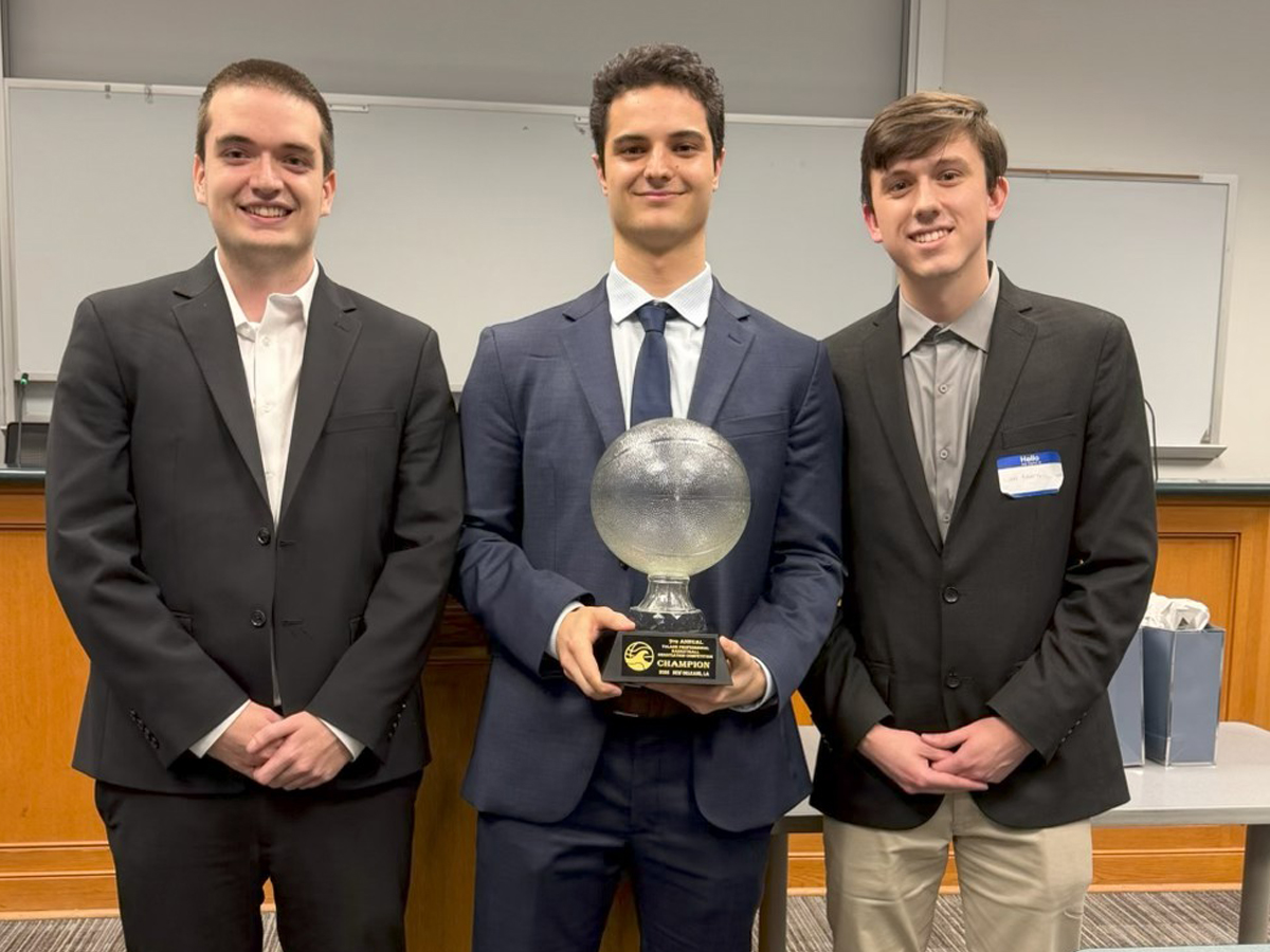 Three students wearing sport coats smile while holding up a first-place trophy.