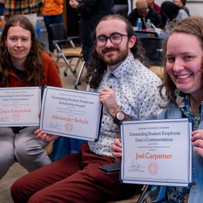Three student employees smile while holding up certificates.