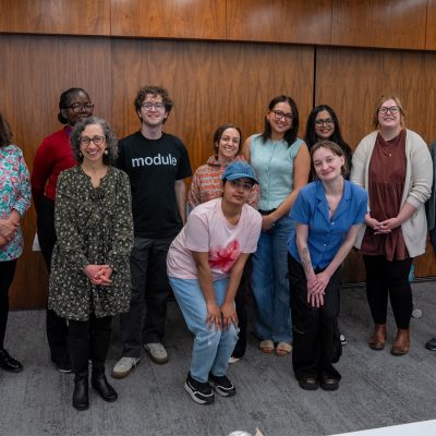 Student Library Advisory Board members and staff members pose for a group photo in front of a wood-paneled wall. The group of 11 includes students and staff standing in two rows, with two members kneeling in front.