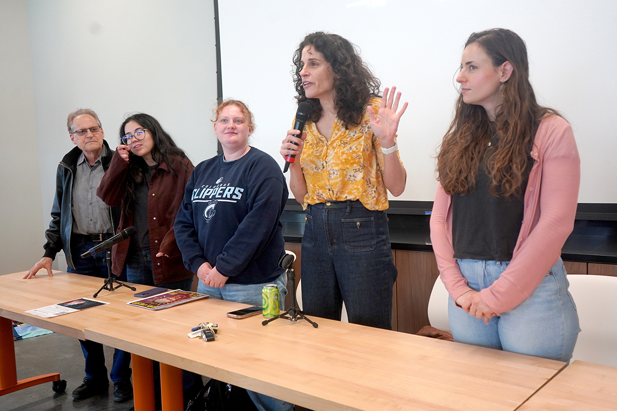 Five panelists stand behind a table at the Engaged Humanities Network Community Showcase as one speaker addresses the audience with a microphone during a discussion on the Engaged Courses initiative.