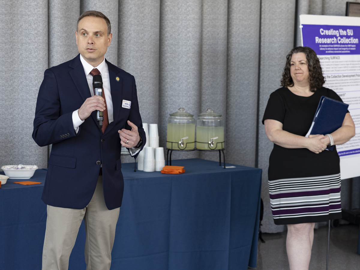 Two professionals address the crowd during an indoor event,