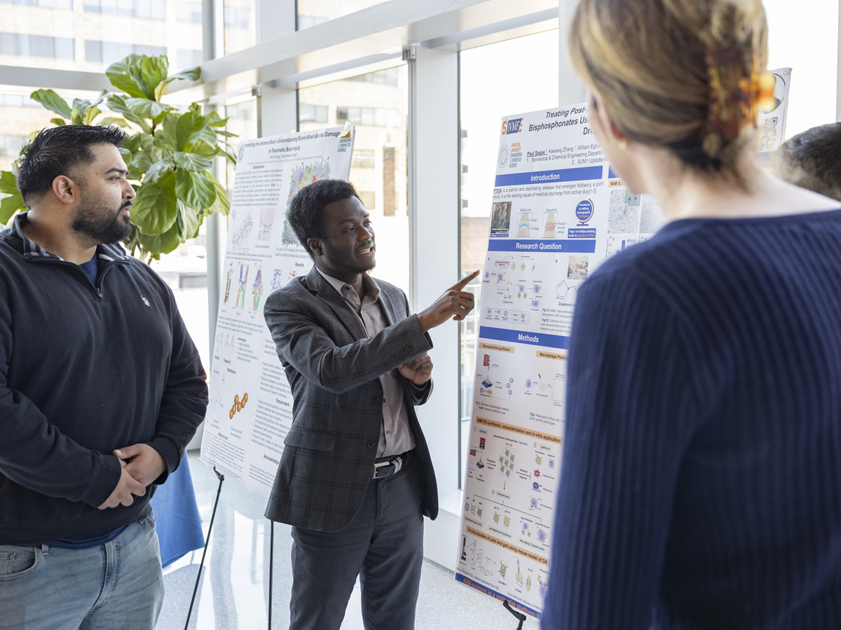 A student points to a research poster on arthritis treatment while presenting to attendees.
