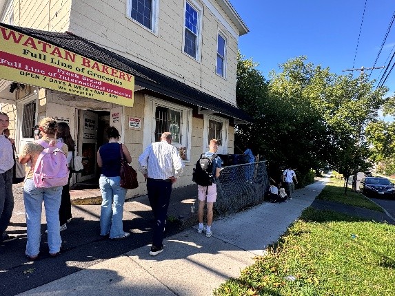Students gather on the sidewalk outside Watan Bakery, a neighborhood grocery and bakery, during a site visit.