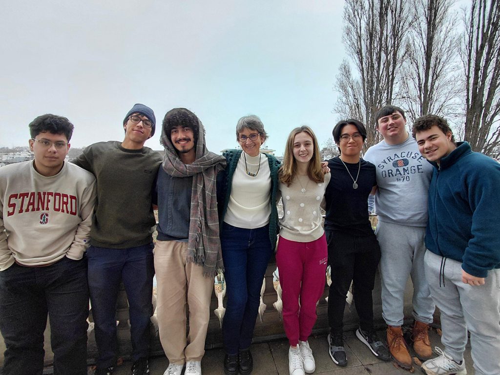 A professor and seven students pose together outdoors on an overcast day, several wearing Stanford and Syracuse University sweatshirts.
