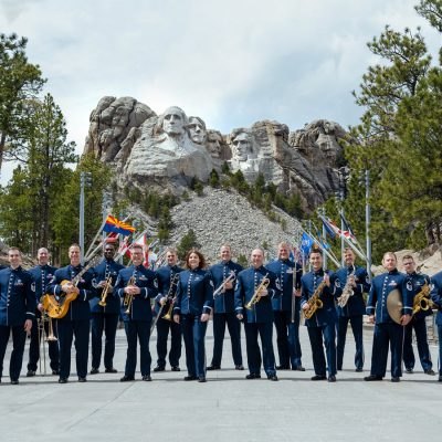 Uniformed military jazz band poses with instruments before Mount Rushmore