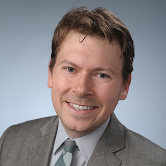 Headshot of person in gray suit and tie against light background, smiling at camera