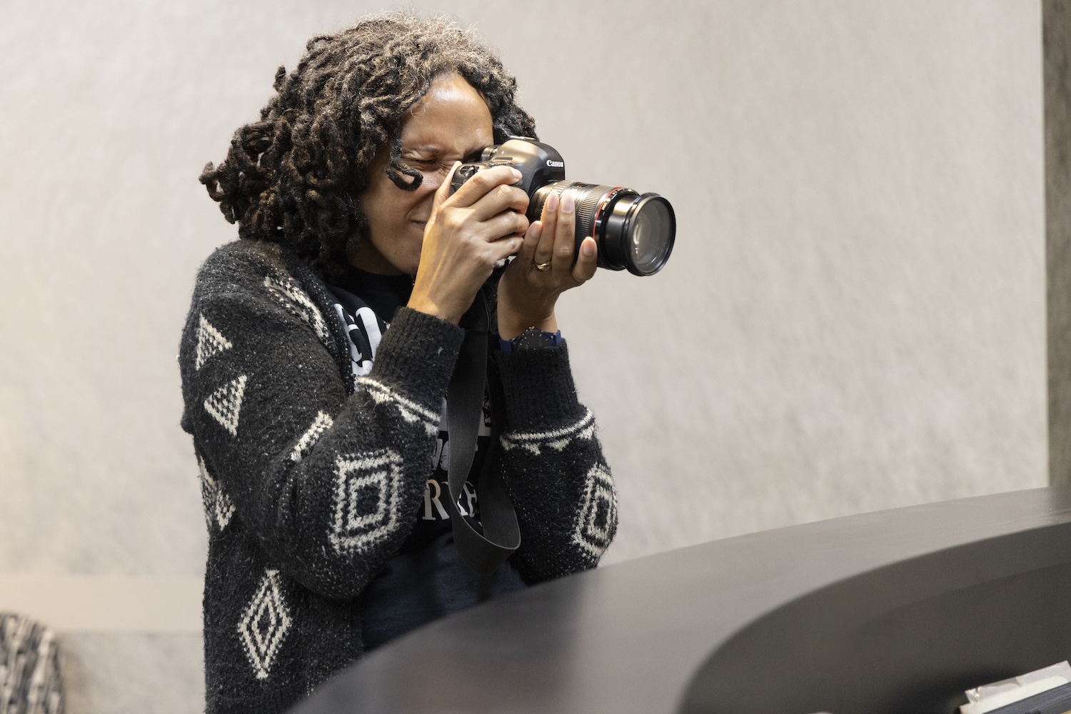 erson holding a camera up to take a photo against a plain indoor wall background.