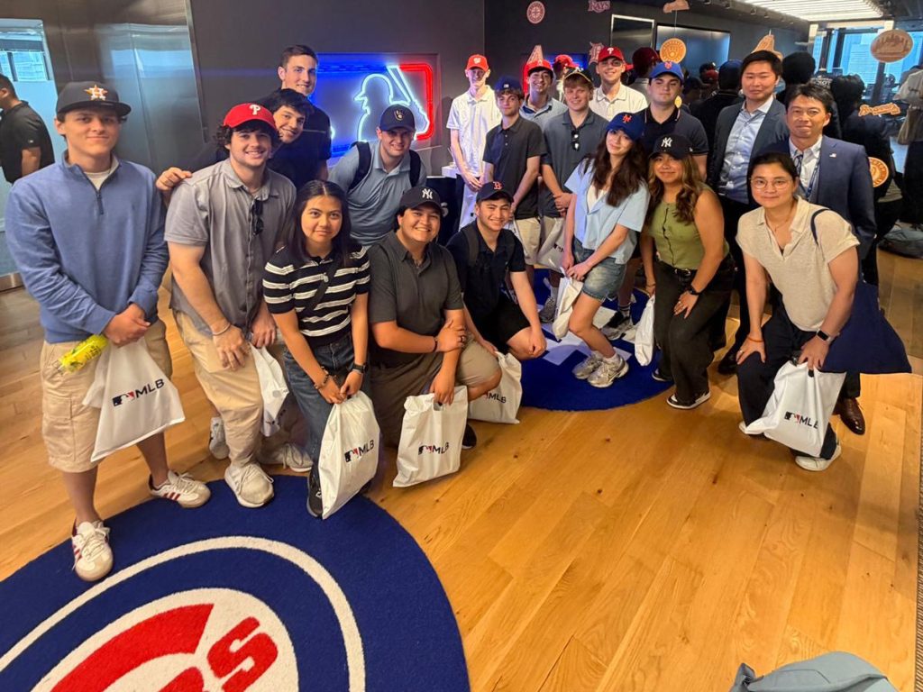 Students and faculty gather at the MLB Asia office, holding MLB gift bags, surrounded by team logos and branded décor.