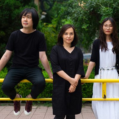 Three people pose outdoors near a yellow railing
