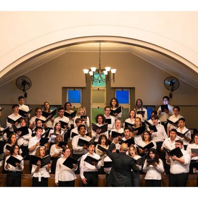 The Hendricks Chapel Choir performs under a vaulted arch at a Dutch Reformed church in Randburg, South Africa, conducted by director José "Peppie" Calvar.