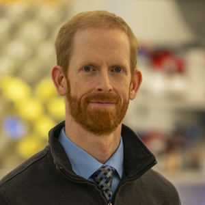 A person stands in a research lab wearing a quarter-zip pullover over a collared shirt and tie.
