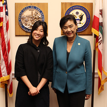 Two women smiling and posing together in front of official government seals and American and California state flags