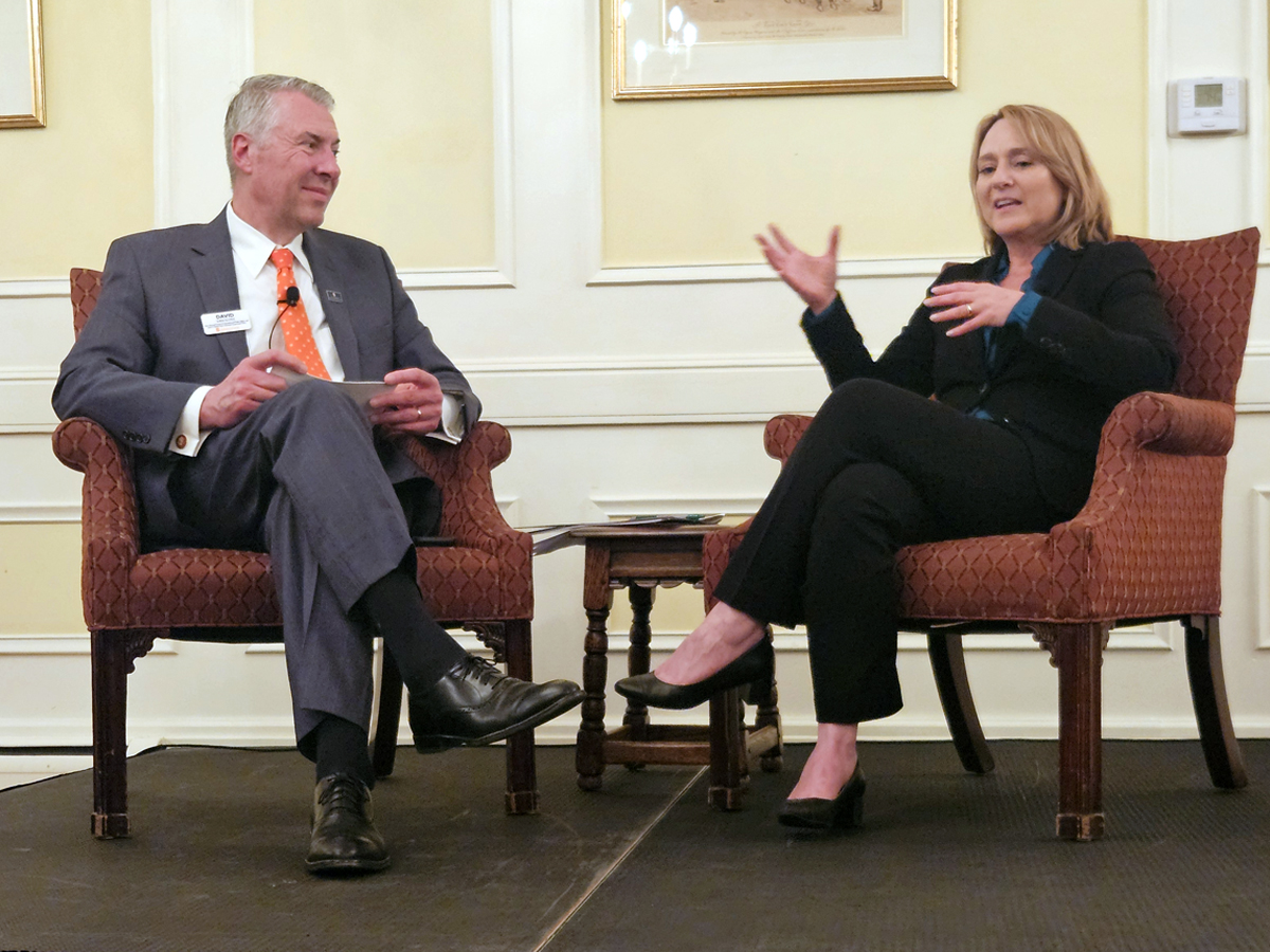 Two people seated in armchairs on a stage engage in a fireside chat-style conversation.