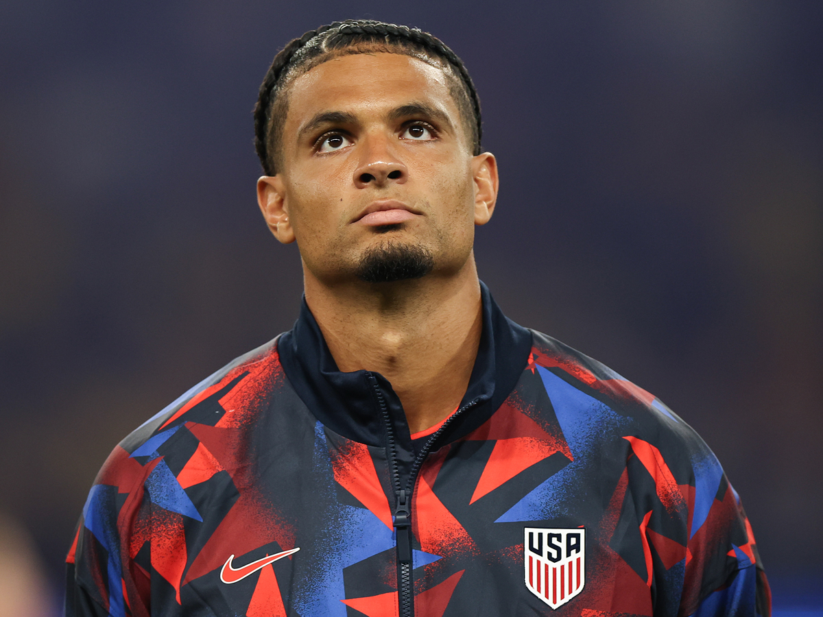 A person stands at attention in a USA warm-up jacket before a national team match.