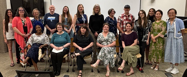 A group of approximately 20 faculty and staff participants in Syracuse University's "On My Own Time" art exhibition pose together for a group photo, with some seated in chairs in front and others standing behind them.