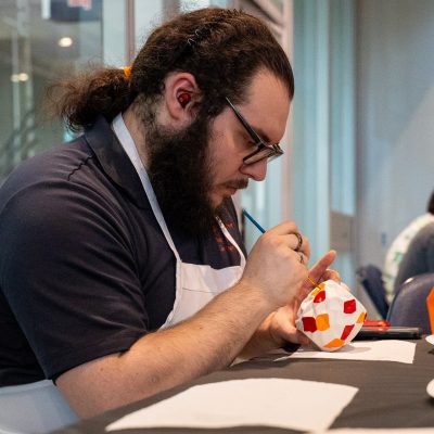 An attendee wearing an apron carefully paints a ceramic pot at a craft activity station during SummerFest at Miron Victory Court in the JMA Wireless Dome.