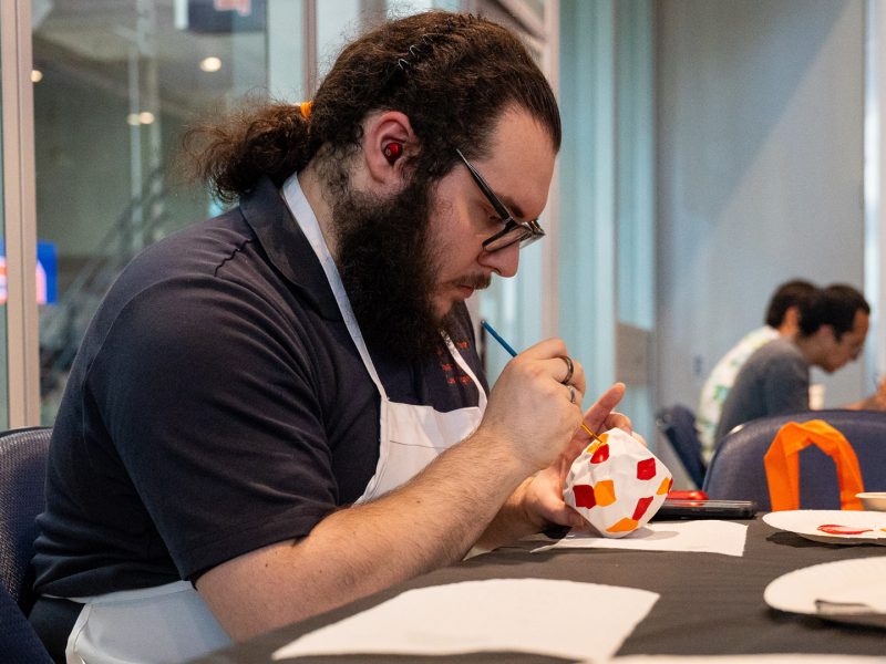 An attendee wearing an apron carefully paints a ceramic pot at a craft activity station during SummerFest at Miron Victory Court in the JMA Wireless Dome.