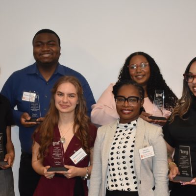 Five smiling students and their faculty mentor pose together holding glass Thursday Morning Roundtable recognition awards against a white background.