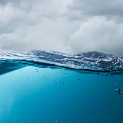 Ocean surface viewed half above and half below water, with blue water, bubbles, and dark storm clouds overhead.