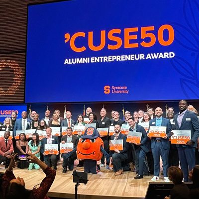'CUSE50 award honorees and Otto the Orange pose onstage under event signage.