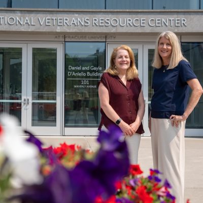 Two people stand outside Syracuse University’s National Veterans Resource Center, with colorful flowers in the foreground.