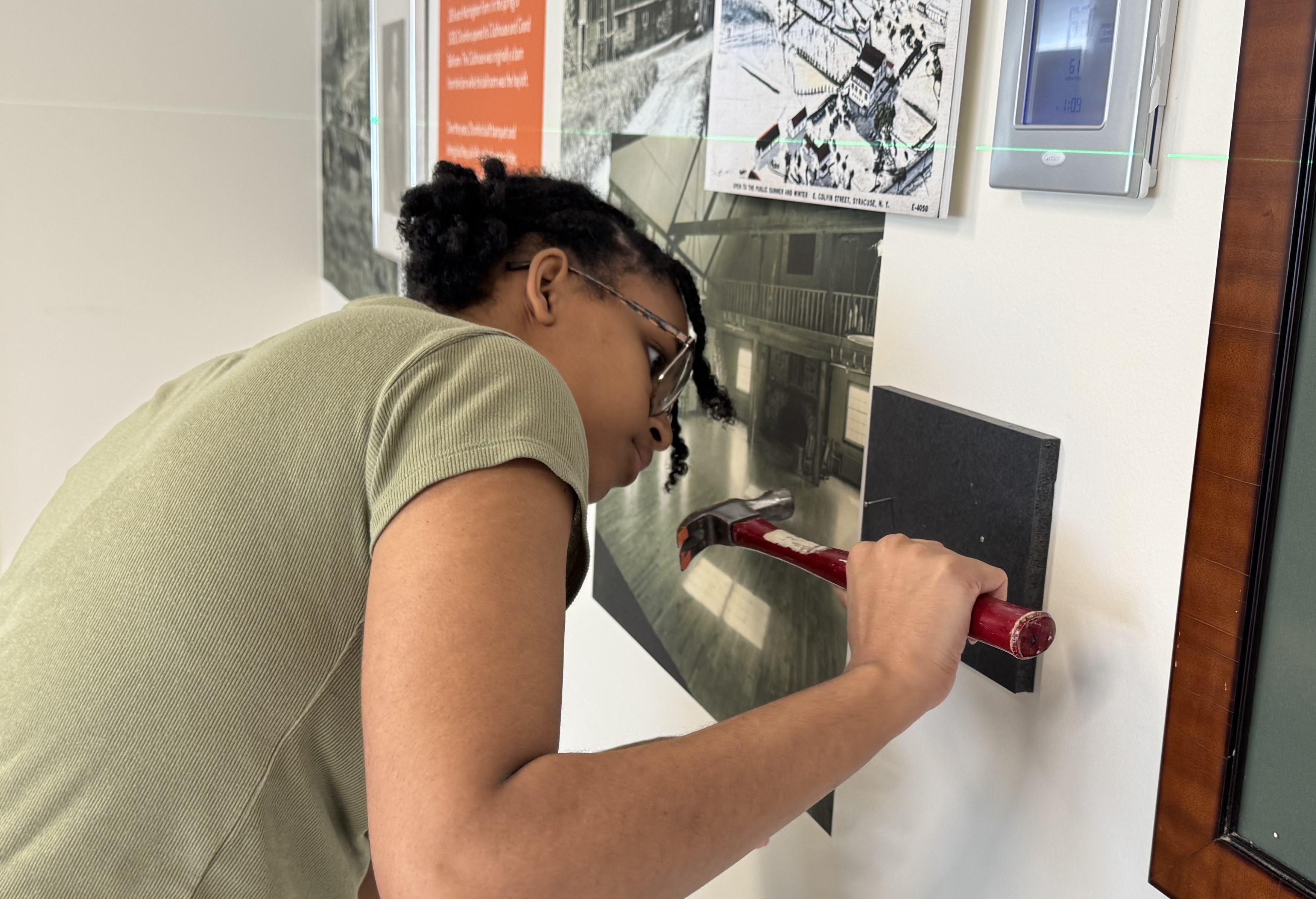 Person using a hammer to interact with a hands-on exhibit mounted on a wall in a museum or educational display area.