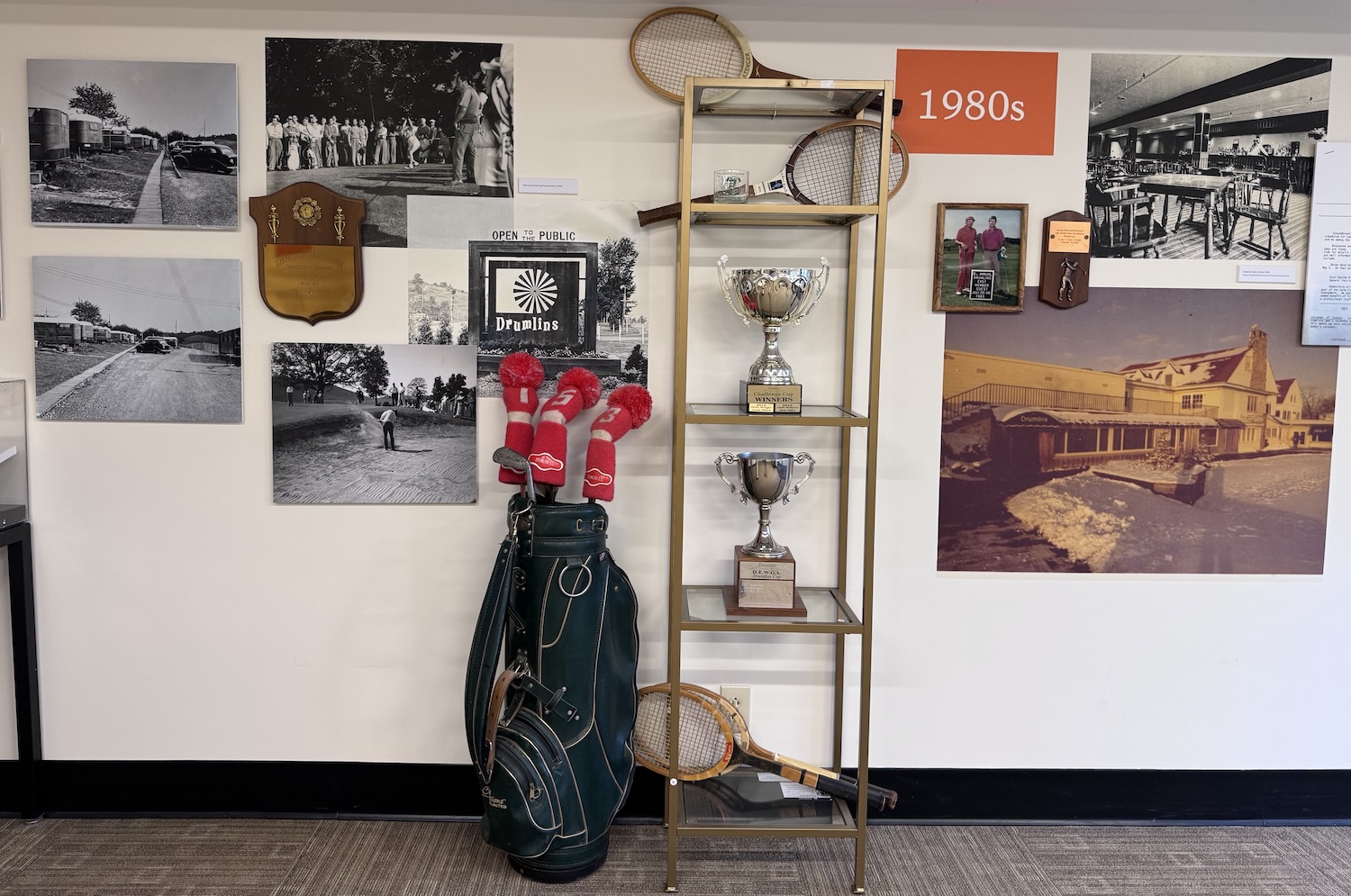 Museum exhibit on Drumlins in the 1980s featuring golf memorabilia, tennis racquets, trophies, and historic photographs.