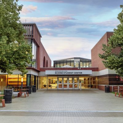 Entrance to the Shine Student Center, a brick campus building framed by trees and a paved walkway.