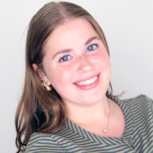 A person smiles while posing for a headshot in front of a white backdrop.
