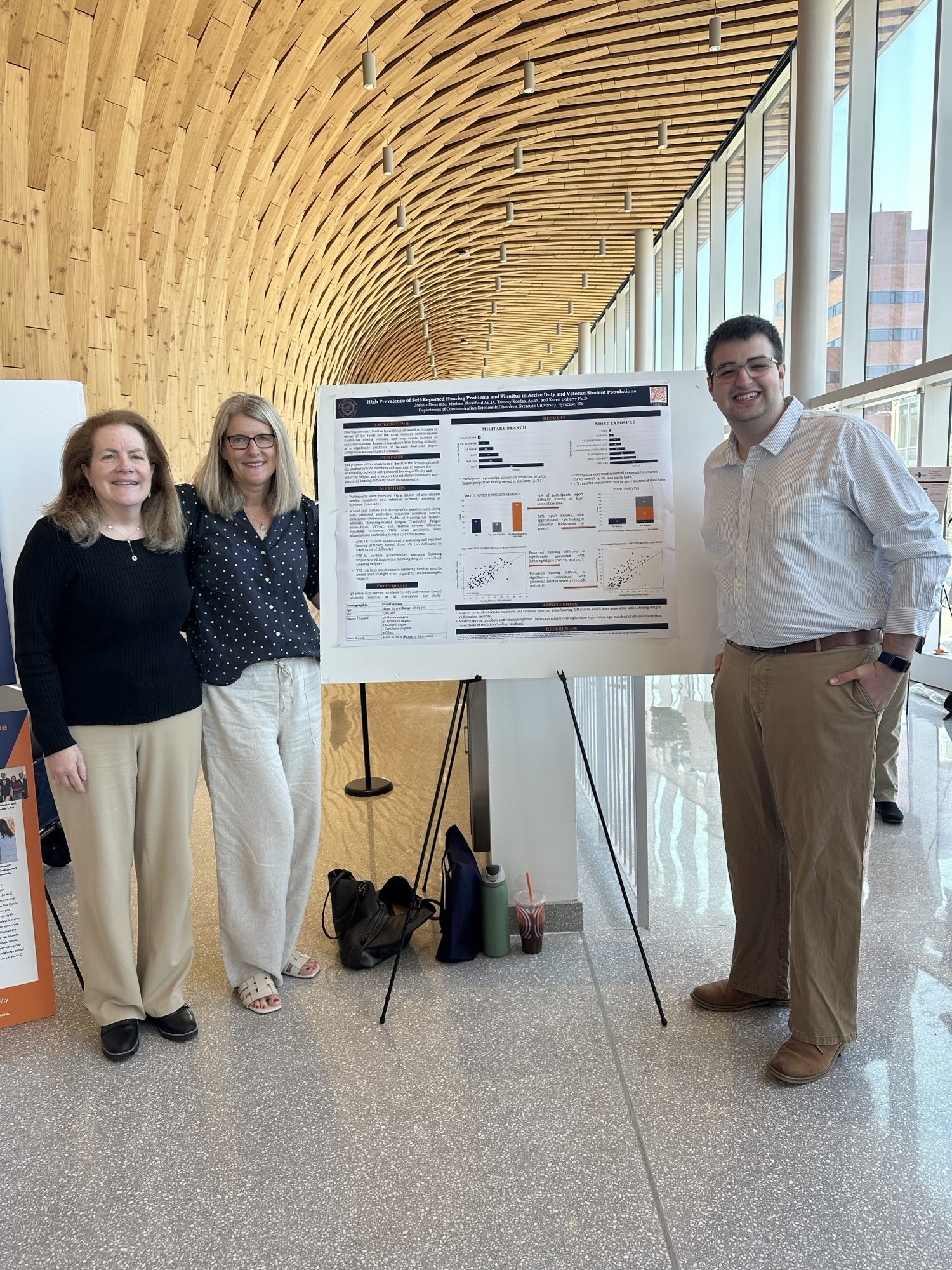 Three people stand beside a research poster on tinnitus among veteran students.