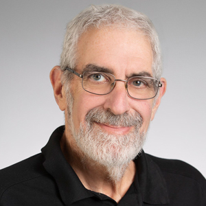 A person smiles while posing for a headshot in front of a grey backdrop.