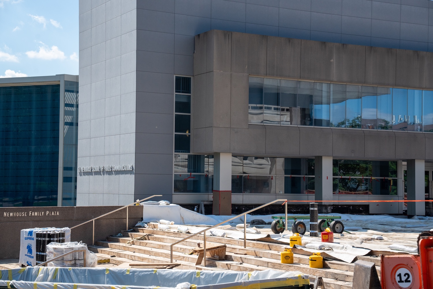 Newhouse Family Plaza under construction outside Newhouse School, with covered walkways, materials, and equipment on site.