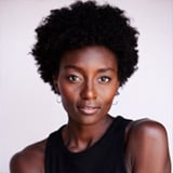 Professional headshot of Bria Huff, a woman with curly black hair, wearing a black top against a light gray background, with a neutral expression.