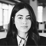 Black and white photo of Giovanna Eisler, a woman with long dark hair, wearing a blazer with a collared shirt, looking directly at the camera with a neutral expression.