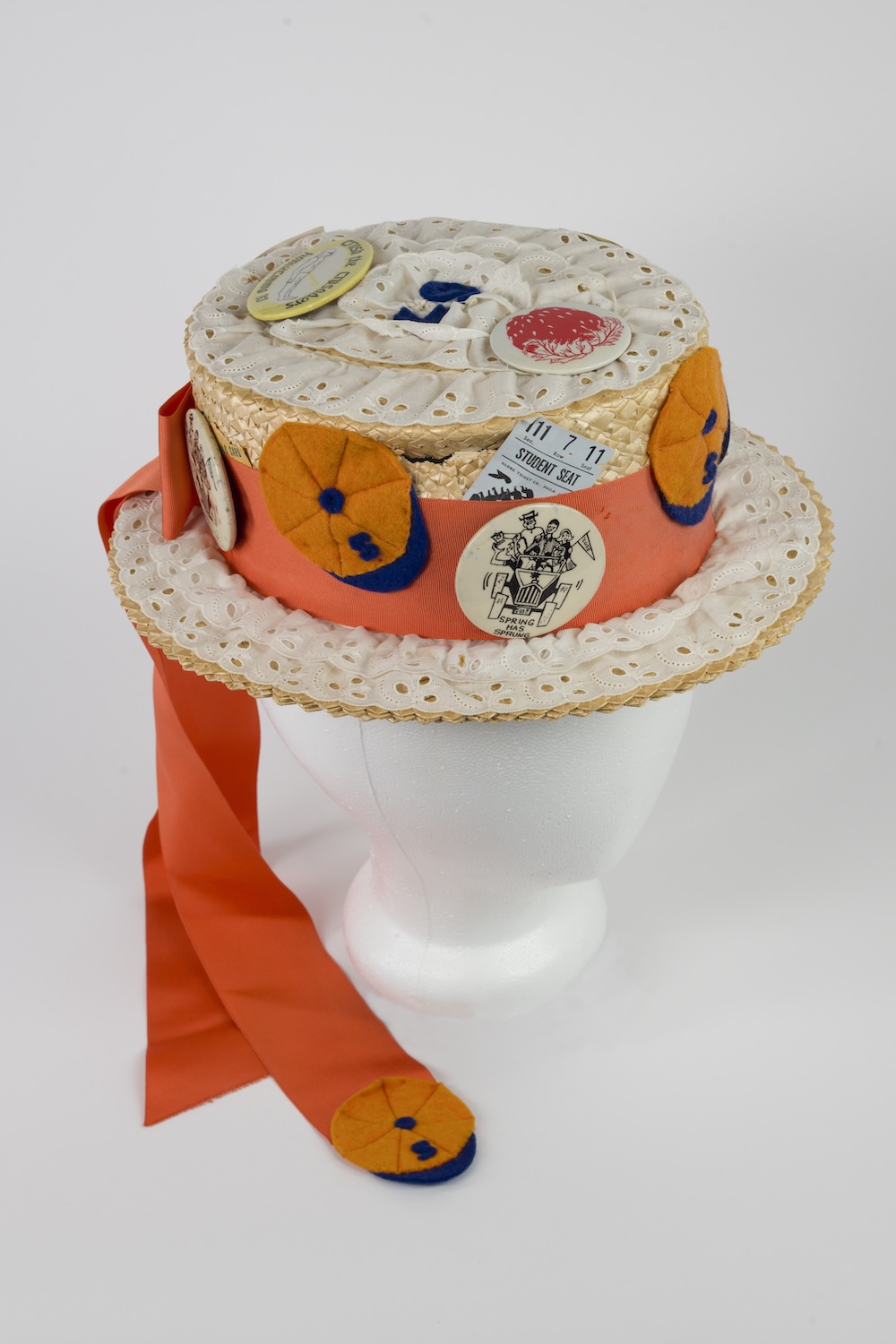 Straw boater hat decorated with lace trim, orange ribbon, felt accents, and commemorative campus event buttons.