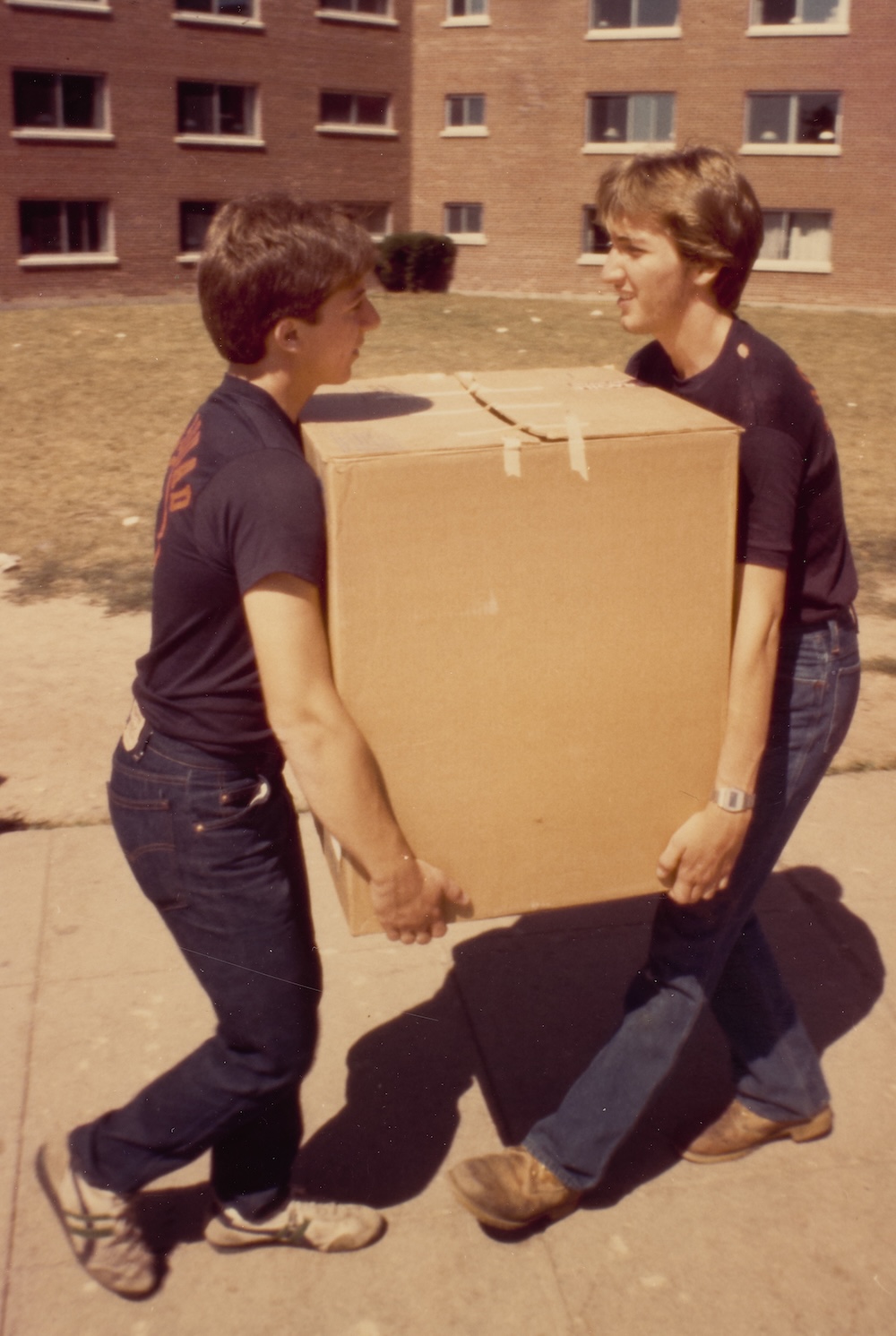 Two volunteers carry a large cardboard box across campus during a residence hall move-in.