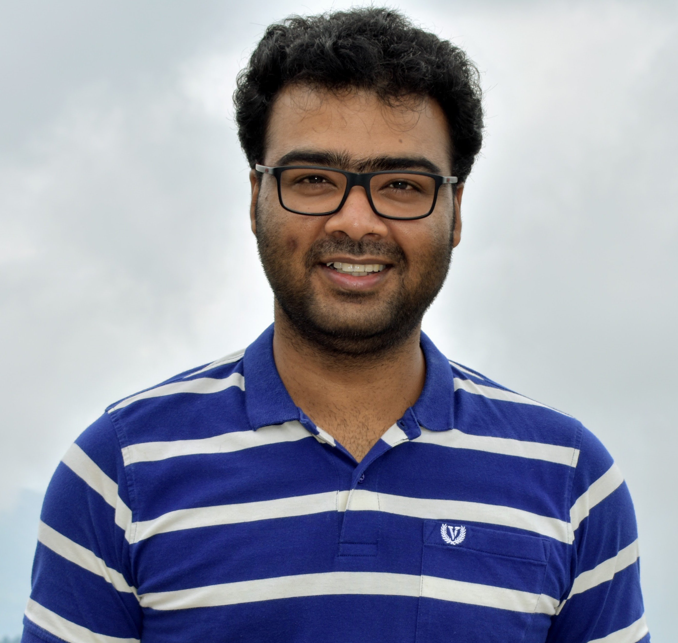 Person wearing glasses and a blue striped polo shirt, standing in front of a softly blurred background.