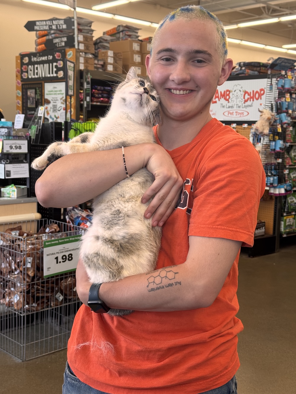 Person holding a cat in a pet store, with shelves of pet supplies in the background.