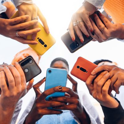 Group of people stand in circle holding smartphones together, viewed from below.