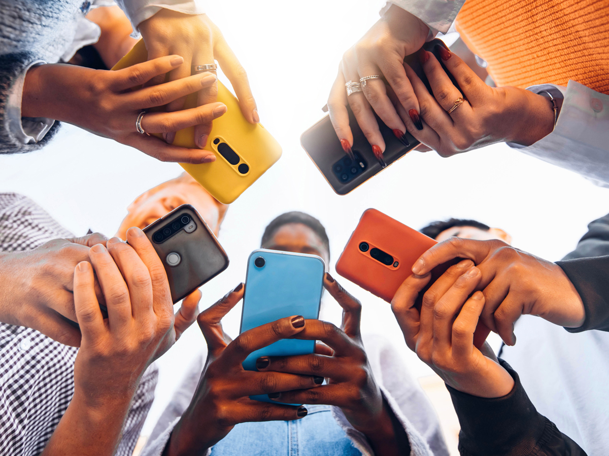 Group of people stand in circle holding smartphones together, viewed from below.