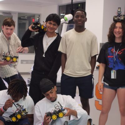 Students in a robotics lab displaying and assembling small wheeled robots during a hands-on engineering activity.