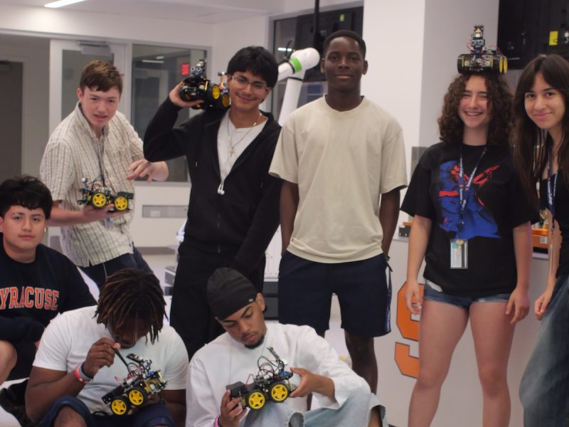 Students in a robotics lab displaying and assembling small wheeled robots during a hands-on engineering activity.