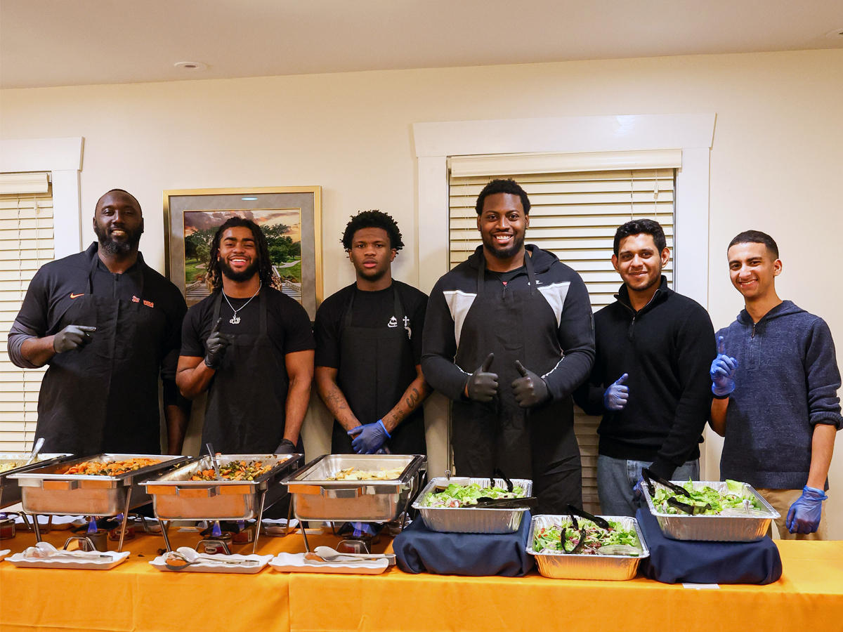 Six individuals pose for a photo in front of food stations.