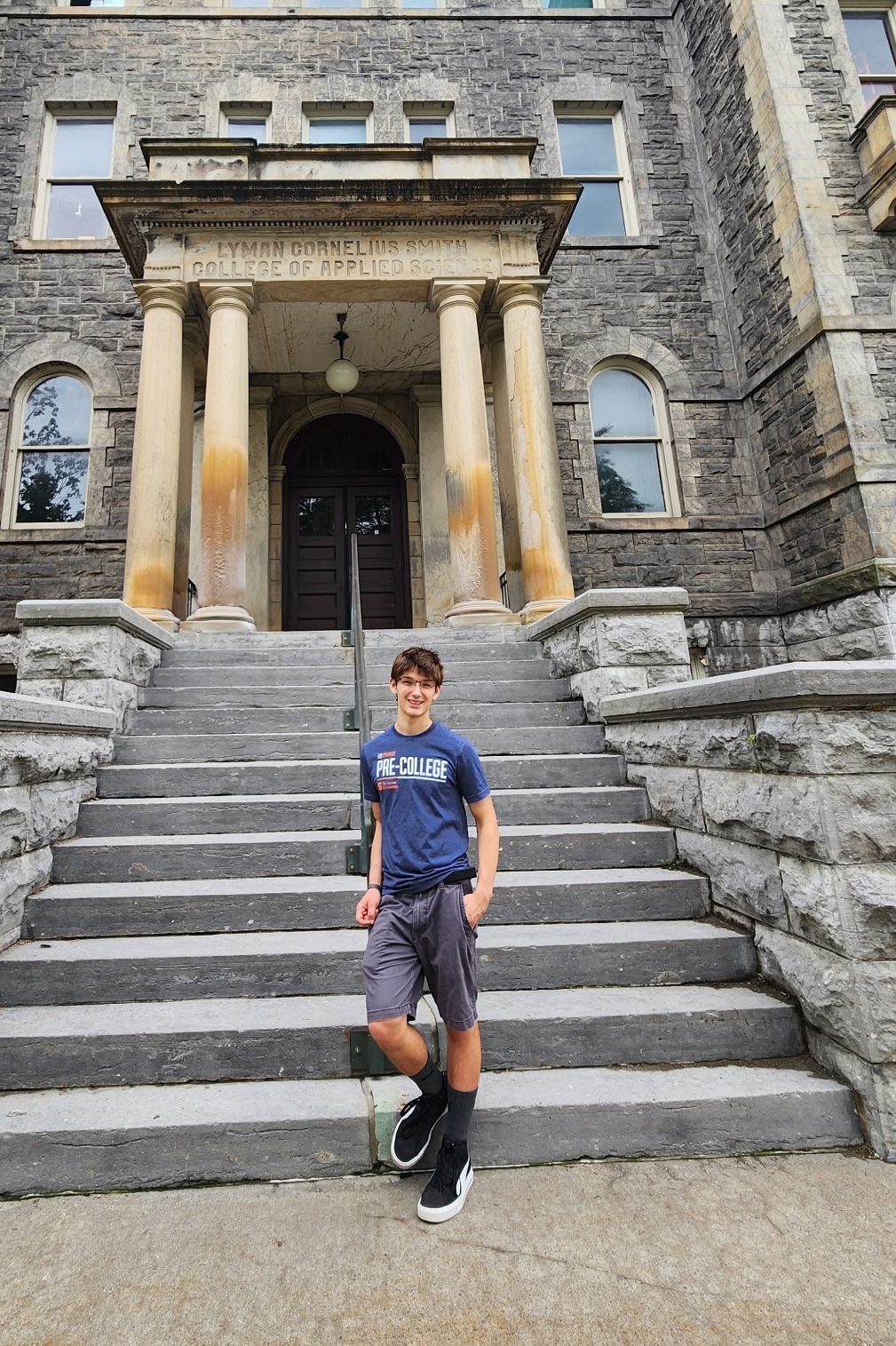 Person standing on the steps of a historic stone academic building.