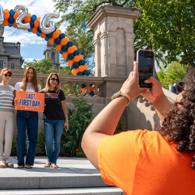 Woman photographs family holding 'Last First Day' sign under 2026 balloon arch
