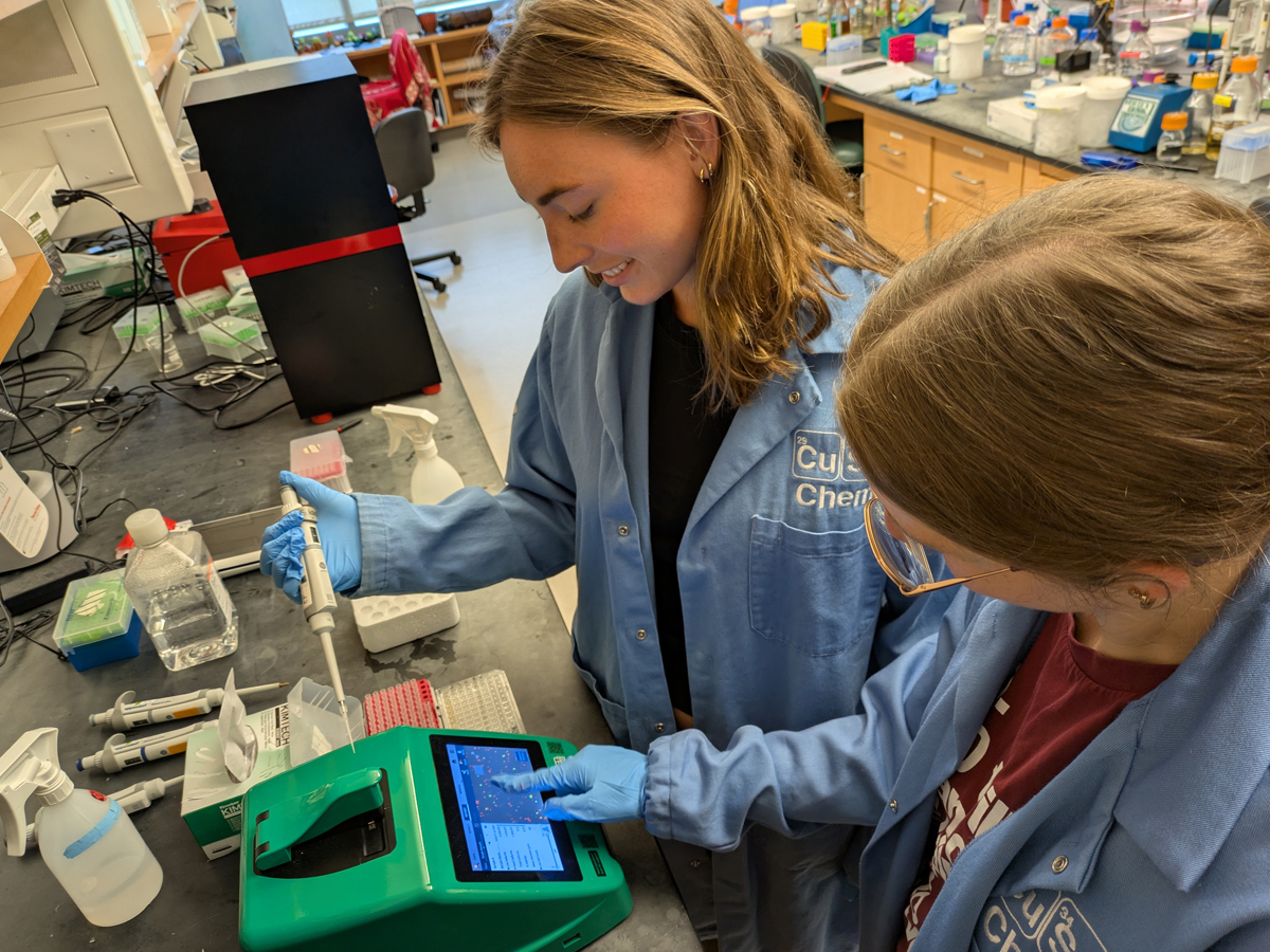 Two students examine data on a lab instrument screen.